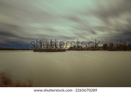 Bird island in the middle of the pond. Time lapse photography. Beautiful clouds blurred by photographic technique - use of ND filter.