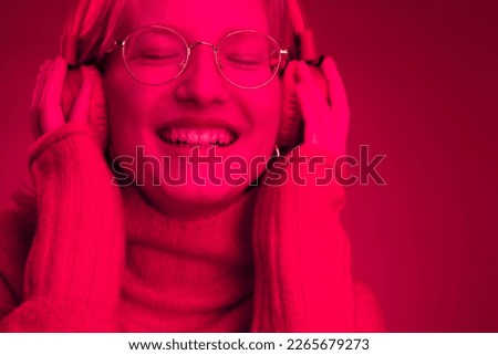 Portrait of a happy girl listening music on headphones isolated on magenta background. Monochromatic picture, viva magenta, color of the year.