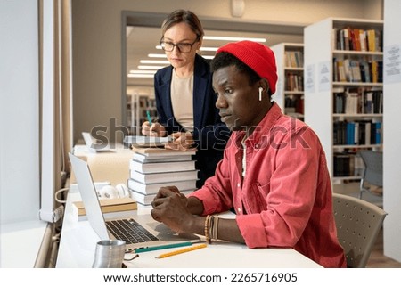 Collaborative learning in higher education. Two diverse students guy and girl using laptop watching webinar, study buddies working on research project together, studying together in University library Royalty-Free Stock Photo #2265716905