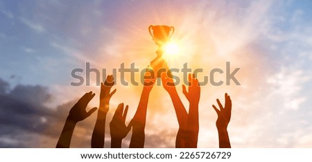 Success of teamwork, joint achievement of goal in business and life. Winning team is holding trophy in hands. Silhouettes of many hands in sunset. Royalty-Free Stock Photo #2265726729