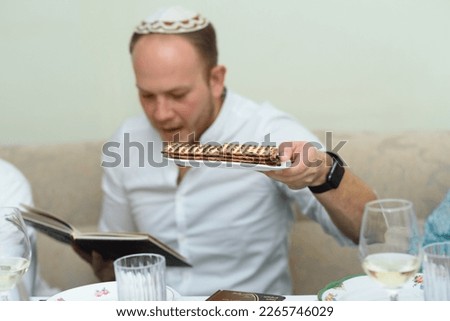 Jewish young man with flatbread Matzah - unleavened flatbread in English is part of Jewish cuisine and forms an integral element of the Passover.Young bearded man reads the Passover Haggadah. Royalty-Free Stock Photo #2265746029