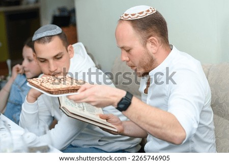Jewish family celebrate Passover Seder reads the Passover Haggadah.Young jewish bearded man with unleavened flatbread in English is part of Jewish cuisine and forms an integral element of the Passover Royalty-Free Stock Photo #2265746905