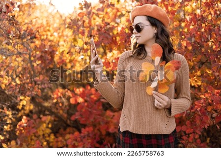 Beautiful young woman in sunglasses with autumn leaves taking selfie with smartphone. Copy space