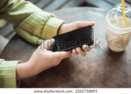 Young woman using phone and computer to make online purchases in shop cafe
