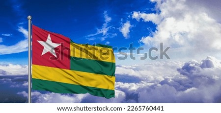 Togo national flag cloth fabric waving on beautiful blue sky.