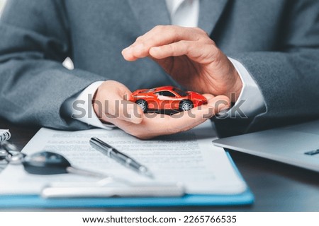 Business woman's hand protecting red toy car on desk. Planning to manage transportation finance costs. Concept of car insurance business, saving buy - sale with tax and loan for new car. Royalty-Free Stock Photo #2265766535