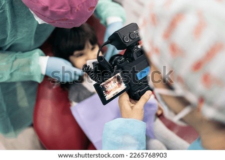 Stock photo of female dentist wearing face mask taking picture of a young patient.