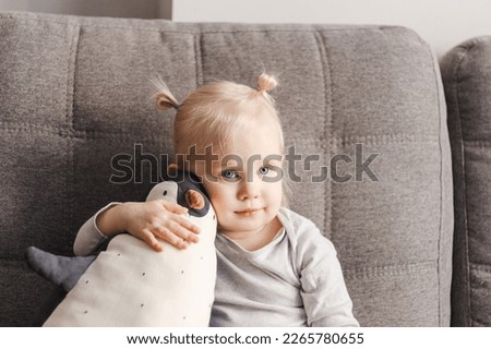 Portrait of a child on a couch with a toy penguin.