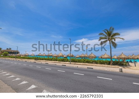 Beautiful coastline view. Sun umbrellas along sand beach on turquoise water and blue sky background. Aruba. 