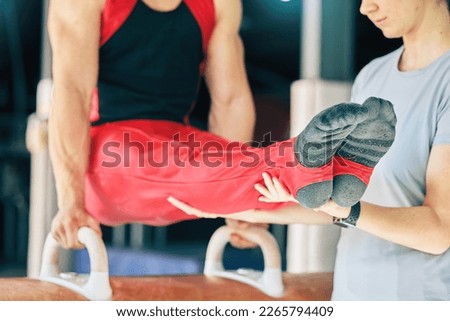Sports, gymnastics and man training on a beam with a coach for balance, flexibility and strength. Fitness, exercise and strong male athlete gymnast practicing for performance or competition at arena.