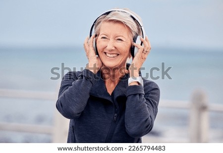 Old woman at beach, headphones and listen to music with smile on face, happiness and freedom outdoor. Fitness, fresh air and technology, podcast or radio streaming with mature female in retirement