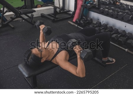A determined middle aged woman with short hair does a set of dumbbell bench presses. Working out chest muscles. Royalty-Free Stock Photo #2265795205