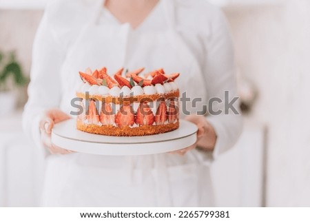 Confectioner in white uniform holding strawberry mousse cake.