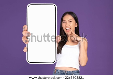 Beautiful Asian brunette woman cute girl in white tank top ,Excited surprised girl showing big smart phone with blank screen , white screen isolated purple background , Mock Up Image
