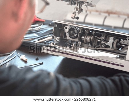 Male master repairs the sewing machine. Inspection of the mechanism in search of a breakdown. Professional adjustment of a sewing machine. Cleaning and repair of professional equipment. Royalty-Free Stock Photo #2265808291