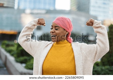 Latina woman, fighting breast cancer, wears a pink scarf, and clenches her arms as a survivor fighter