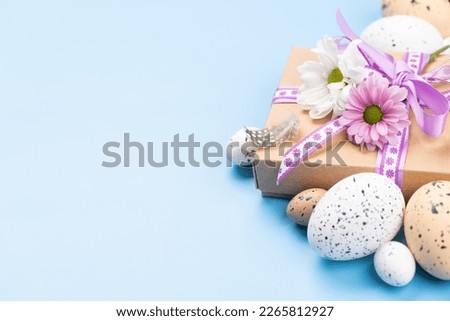 Gift box, Easter eggs and flowers on a blue background with space for your greetings