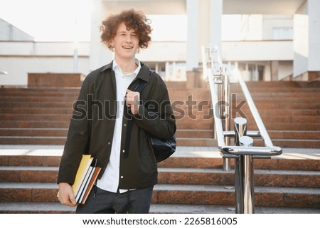 University.Smiling young student man holding a book and a bag on a university background .Young smiling student outdoors Life style.City.Student