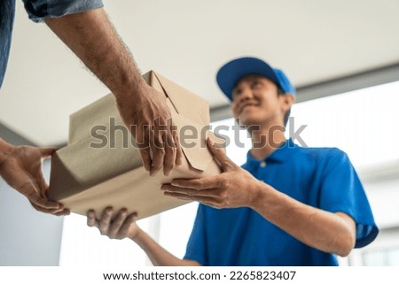 Asian delivery man with parcel in hand of blue uniform sending parcel to customer front of the house from shopping online with good service. Courier man send a package to destination. Royalty-Free Stock Photo #2265823407