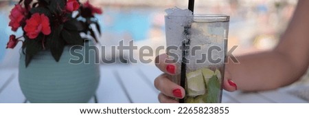 Beautiful glass with refreshing cocktail in woman hand on background of pool