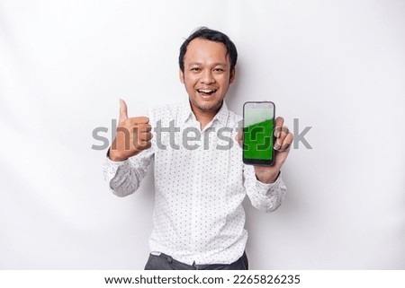 A portrait of a smiling Asian man wearing a white shirt and showing green screen on her phone, isolated by white background