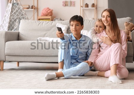 Mother with her little children watching cartoons on TV at home