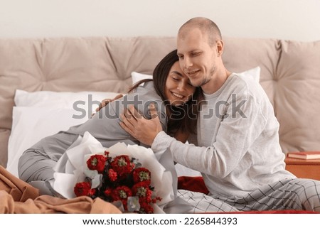 Young couple with flowers hugging in bedroom on Valentine's Day