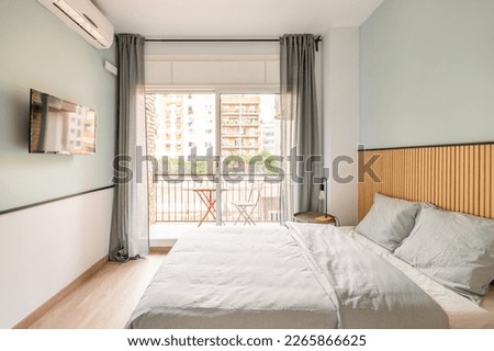Spacious bright room with bed, large opening on entire wall with sliding plastic doors and access to balcony. Room has table with chair, air conditioning and TV for pleasant leisure. Royalty-Free Stock Photo #2265866625