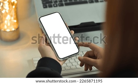 Unrecognizable woman hands holding smart phone with white screen. Over shoulder closeup view, selective focus on phone