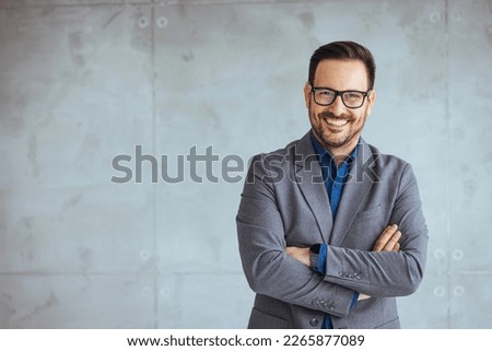 Businessman smiling with arms crossed on white background. Portrait of young happy businessman wearing grey suit and blue shirt standing in his office and smiling with arms crossed
