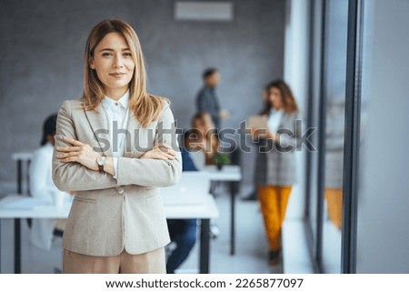 Portrait of businesswoman with a file standing in meeting room with colleagues disucssing in background. Waist up portrait modern business woman in the office with copy space