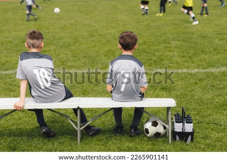 Two School Boys in Sports Football Team. Kids in Classic Soccer Jersey Uniforms With Numbers. Kids Playing Sports Together. Children Resting and  Sitting on Sideline Substitute Bench Royalty-Free Stock Photo #2265901141