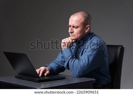 Mature businessman sitting at his desk working on laptop, on gray background