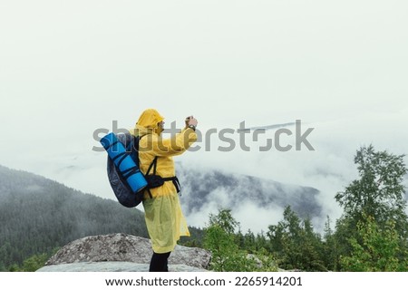 Male hiker in a yellow raincoat takes photos of beautiful mountain views on a smartphone camera