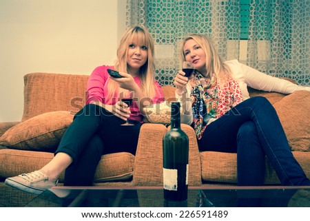 best friends - 2 girls enjoy watching tv at home drinking a glass of wine retro style filtered stock photo