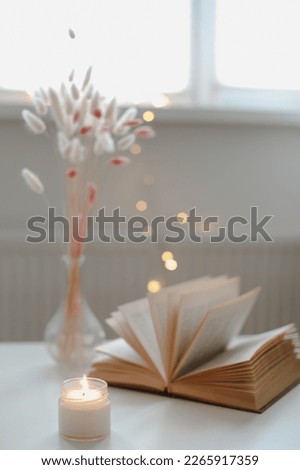 Home decoration and interior. Beautiful burning candle with dry flowers in a vase and an open book