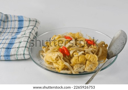 Stir-fried vegetables with bean sprouts and tofu served in a small plate with a napkin, a spoon,  and isolated on a white background.