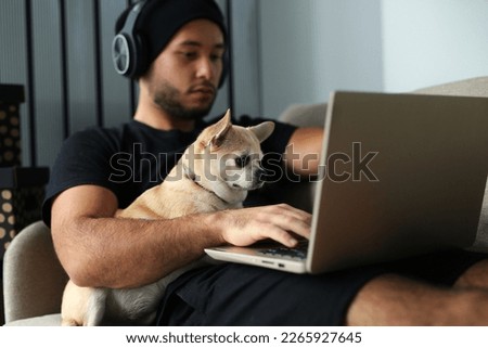 A stylish man in black clothes is at home, the guy works, watches a movie, studies on a computer. With a guy at home, a Chihuahua dog, a faithful friend and helper