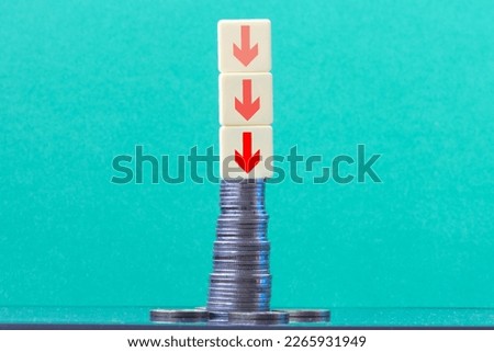 Stack of coins red arrows trending downwards with green wall background on  table copy space. Economy recession crisis, inflation, stagflation, business and financial loss concept.
