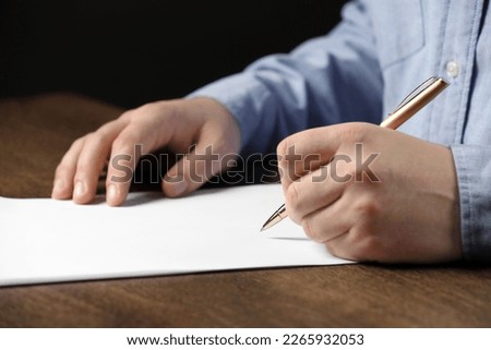 Man writing on sheet of paper with pen at wooden table, closeup