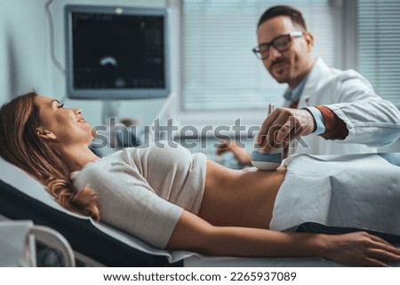 Pregnant woman undergoing ultrasound test at gynecologist office. Closeup of male doctor moving ultrasound probe on pregnant woman's stomach in hospital. Doctor and patient. Ultrasound equipment. 