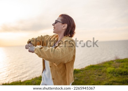 Hqppy woman posing against the background of water and grass. Female raised her hands up