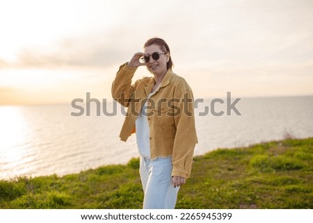 Hqppy woman posing against the background of water and grass. Female raised her hands up
