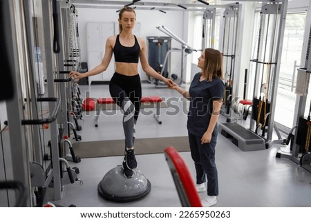 Physiotherapist helping female patient with rehabilitation. Balance exercise with bosu ball. Woman and doctor during rehab physiotherapy in gym