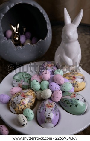 photo bright decorative large and small eggs lie on a special plate and next to a white rabbit on a round glass table