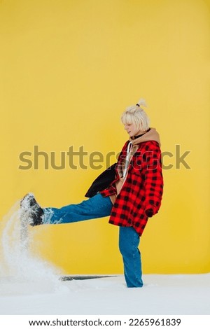 Positive woman in casual clothes standing on snow street zi on yellow background and having fun.