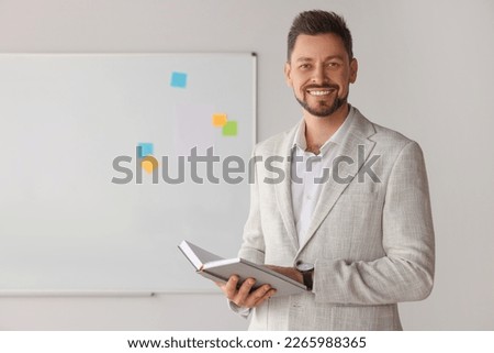 Happy teacher with book at whiteboard in classroom Royalty-Free Stock Photo #2265988365