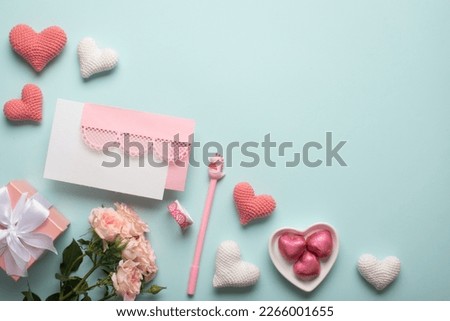 A banner with a gift, a bouquet of roses, an envelope, tape, a pen and knitted hearts on a light blue background. An invitation for Valentine's Day. Space for copying. Flat position, top view.