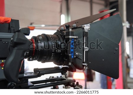 The front of a professional video camera with a mounted cinema lens and a compendium