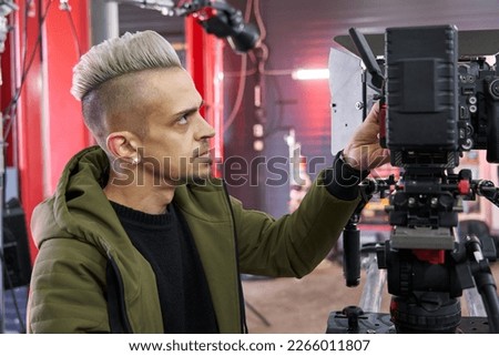 handsome caucasian man with mohawk haircut operating a professional movie camera on set
